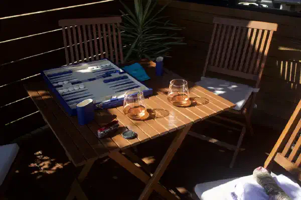 A backgammon board, prepared for play on an outdoor patio table. Two drinks are also on the table.