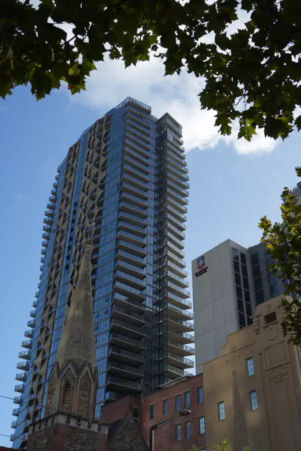 A tall city building, with a small church steeple in the foreground