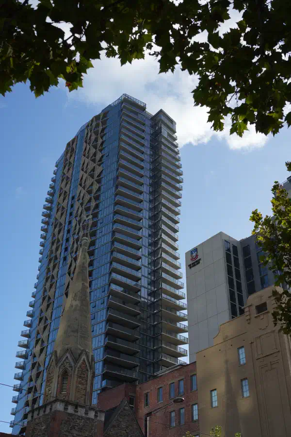 A tall city building, with a small church steeple in the foreground