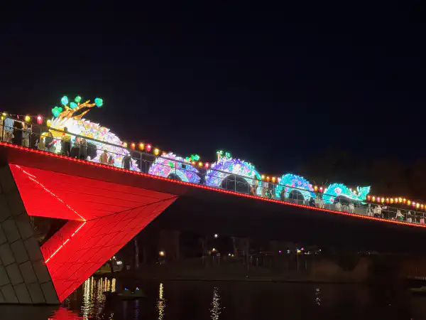 A Chinese dragon installation atop a bridge at night-time. It is lit from within. It has many vibrant colours