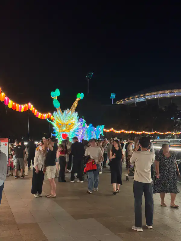 A Chinese dragon installation atop a bridge at night-time. It is lit from within. It has many vibrant colours