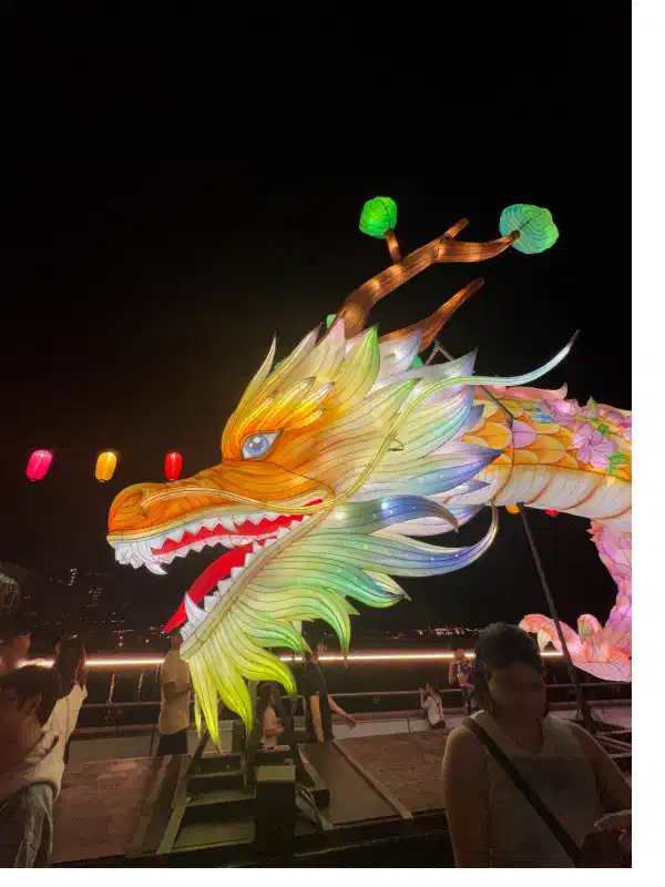 A Chinese dragon installation atop a bridge at night-time. This is a close-up of its colourful, large head.