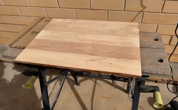 A tabletop on a sawhorse, freshly sanded to raw wood